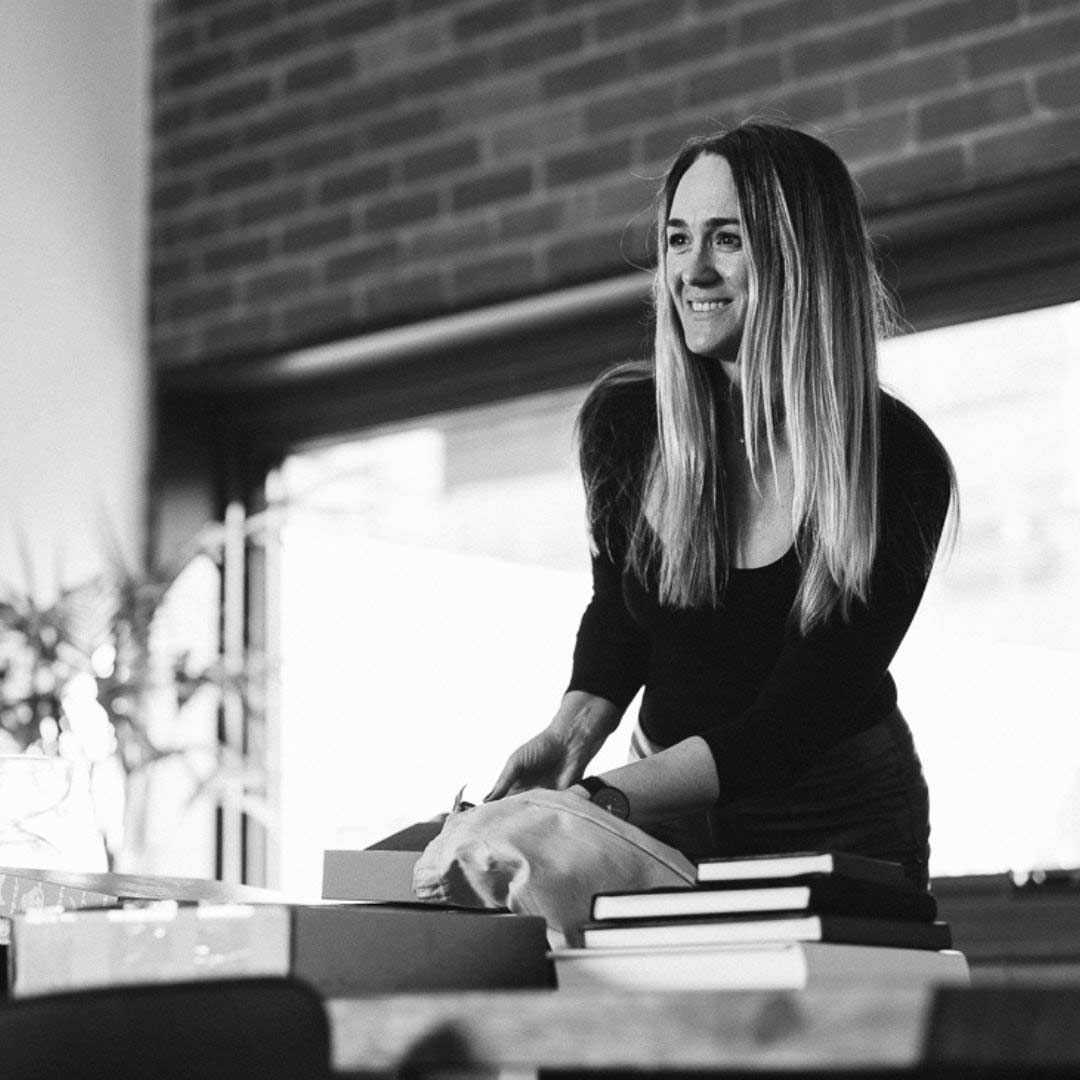 Business owner in a black top smiling as she leans over a studio table stacked with hardcover albums and lidded presentation boxes